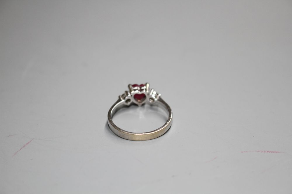 A modern 750 white metal, claw set heart shaped ruby and two round cut diamond set dress ring,